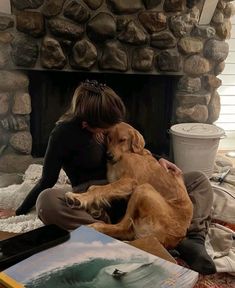 a woman sitting on the floor with her dog in front of a stone fire place