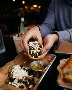 a person holding food in their hand while sitting at a table with other foods on it