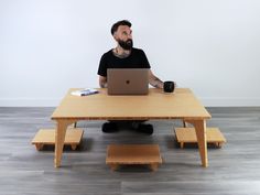 a man sitting at a wooden table with a laptop and coffee cup in front of him