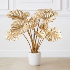 a white vase filled with gold leaves on top of a wooden table