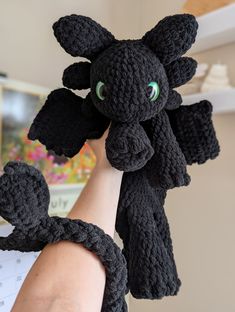 a person holding up a black crocheted toy