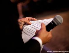 a person holding a microphone in their left hand while reading a piece of paper with writing on it