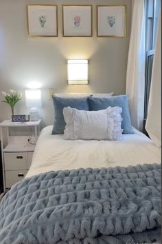 a white bed with blue pillows and blankets on it in front of three framed pictures