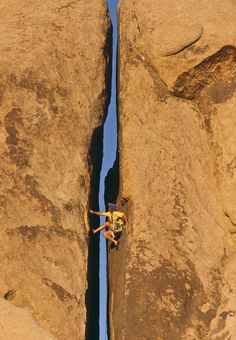 a man climbing up the side of a large rock in front of a blue sky