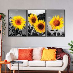 three sunflowers in black and white on a wall above a couch with orange pillows