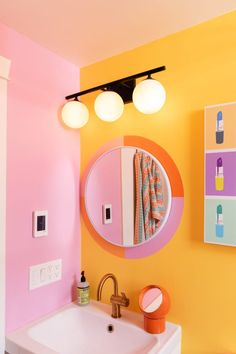 a bathroom with yellow and pink walls and a round mirror on the wall above a white sink