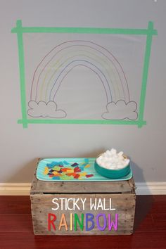 a wooden box sitting on top of a floor next to a wall with a rainbow drawn on it