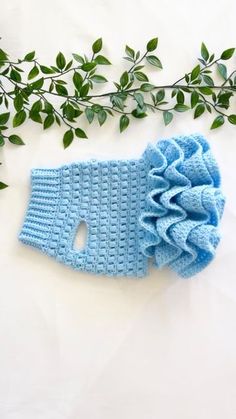 a blue crocheted headband with a flower on it next to some green leaves