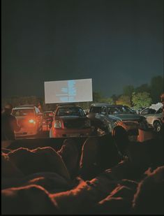 cars are parked in a parking lot at night with a projector screen above them