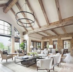 a living room filled with lots of furniture next to large windows and a chandelier hanging from the ceiling