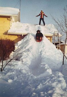 a man riding a snowboard down the side of a pile of snow next to a house