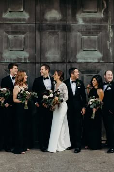 a group of people standing next to each other in front of a metal wall holding bouquets