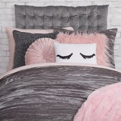 a bed with pink and grey pillows and a white pillow on it's side