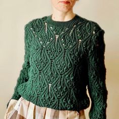 a woman is wearing a green sweater and plaid skirt with her hands in her pockets