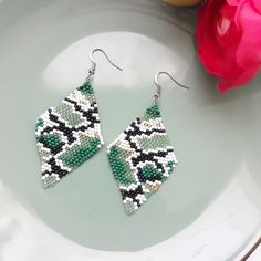 a pair of green and white beaded earrings sitting on top of a plate next to a pink flower