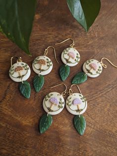 six earrings with flowers and leaves on them sitting on a table next to a plant