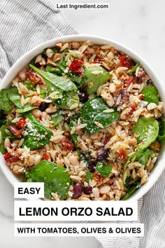 a white bowl filled with lemon orzo salad and topped with tomatoes, olives and greens