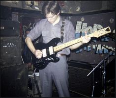 a young man playing an electric guitar in a room with other guitars and amps