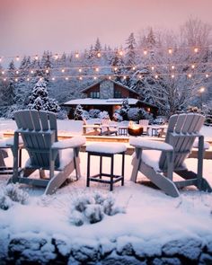 four adiron chairs sitting in the snow with lights strung over them and trees behind them