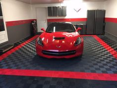 a red sports car is parked in a garage with checkered flooring and cabinets