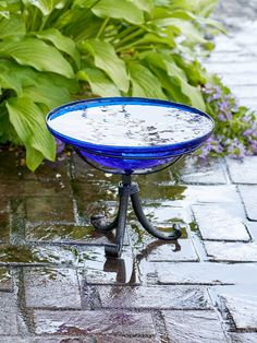 a blue glass bowl sitting on top of a metal stand in front of some flowers