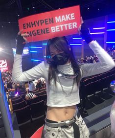 a woman holding up a sign that says enhypen make genee better in front of an audience