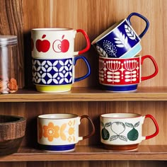 three colorful coffee mugs sitting on top of a wooden shelf