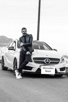 a man sitting on the hood of a car next to a sign that says mercedes benz