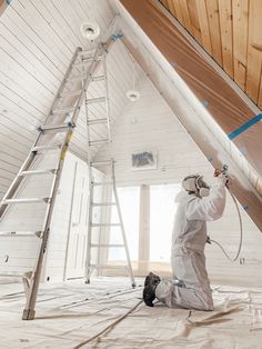 a man painting the ceiling in a room with white walls and wooden ceilings, while another man is on a ladder nearby