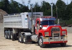 a red and white dump truck driving down a dirt road