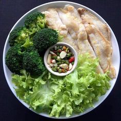 a white plate topped with fish and veggies next to a bowl of sauce