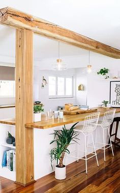 a kitchen with wooden flooring and white walls is pictured in this image, there are three chairs at the bar