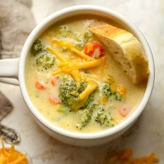 a white bowl filled with broccoli cheese soup and bread on top of a table