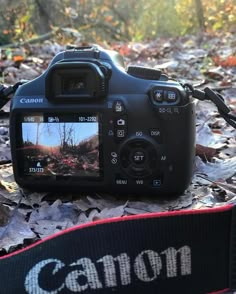 a canon camera sitting on the ground with leaves around it and its reflection in the lens