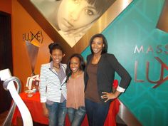 three women standing in front of a sign for massage luv with an advertisement on the wall behind them