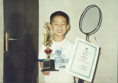 a young boy holding up a trophy next to a plaque and a tennis racket