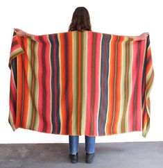 a woman holding up a multicolored blanket in front of her back to the camera