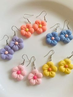 six different colored flower earrings on a white plate