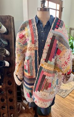 a mannequin wearing a multicolored jacket next to a wine rack filled with bottles