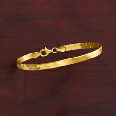 a gold bracelet on a wooden surface with a knot at the end and an oval clasp in the middle