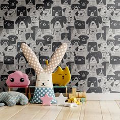 two stuffed animals sit on the floor in front of a wall with dogs and cats