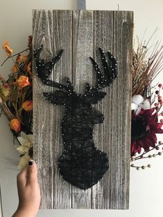 a person holding up a piece of art made out of string and wood with an image of a deer on it