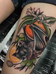 a tattoo with a bat and an orange on the side of her leg that has flowers around it