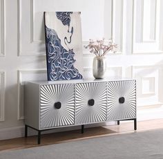 a white vase sitting on top of a wooden cabinet next to a painting and flowers