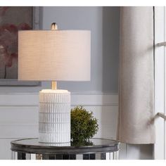 a white table lamp sitting on top of a glass table next to a window with curtains