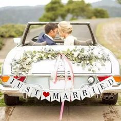 a bride and groom sitting in the back of a convertible car with just married banner