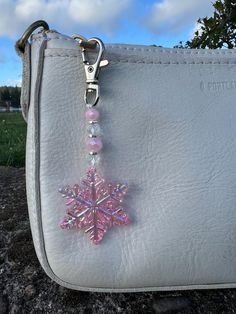 a white purse with a pink snowflake charm hanging from it's side