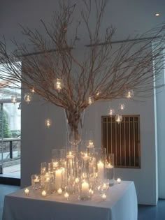 a vase filled with lots of candles sitting on top of a table covered in branches