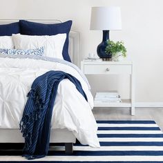 a white bed with blue and white comforter in a bedroom next to a night stand