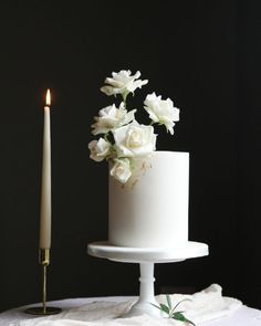 a white cake sitting on top of a table next to a candle and some flowers